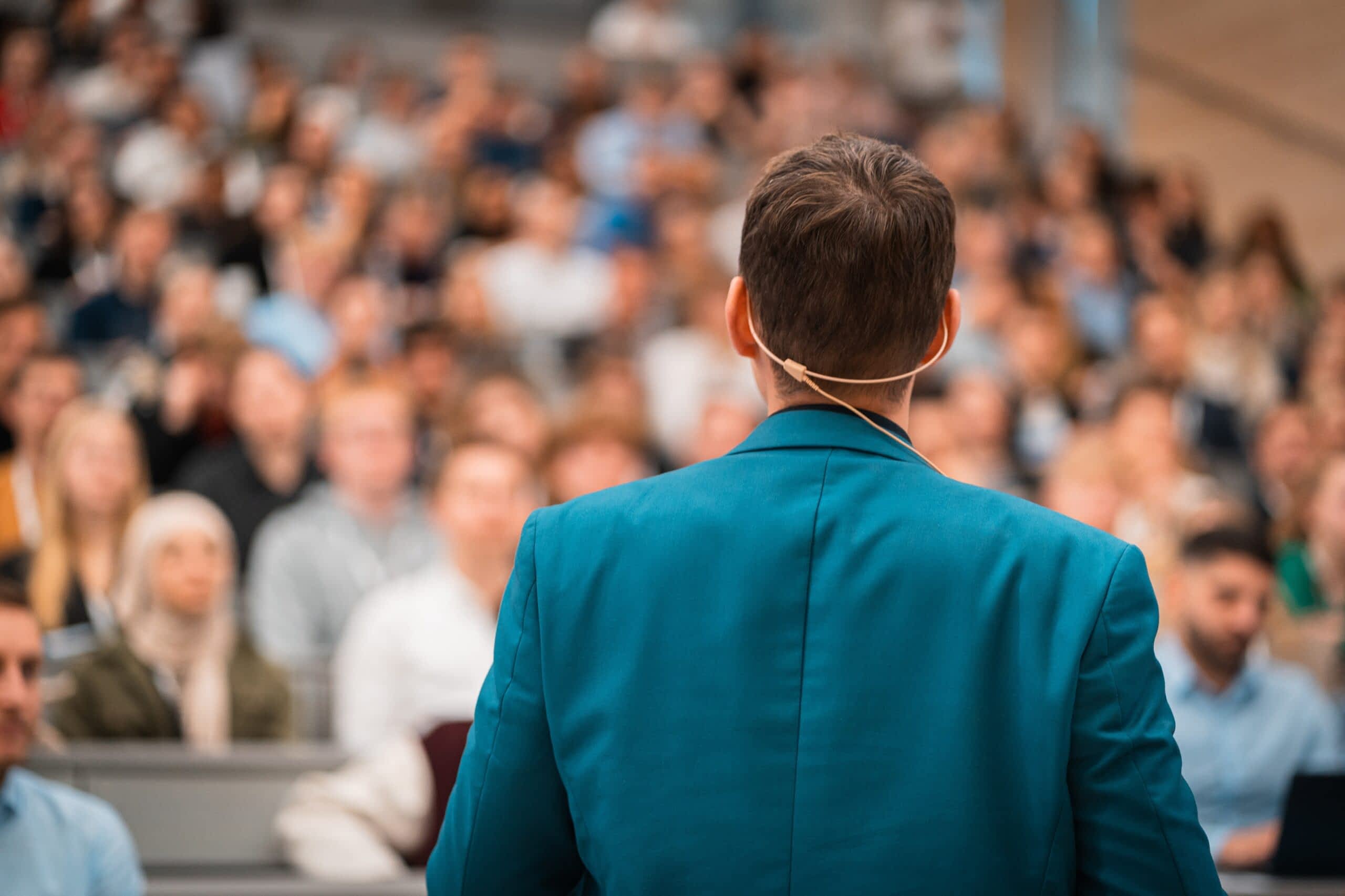 Der Referent des Events steht im Fokus. Die Teilnehmenden des Events lauschen im im Hintergrund